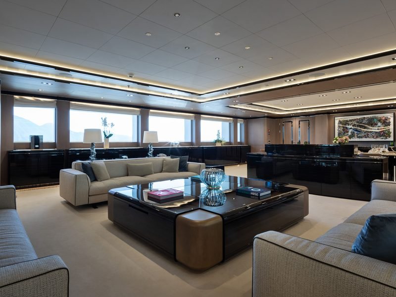 Main saloon with pale sofas around a dark lacquer table beneath ribbon windows