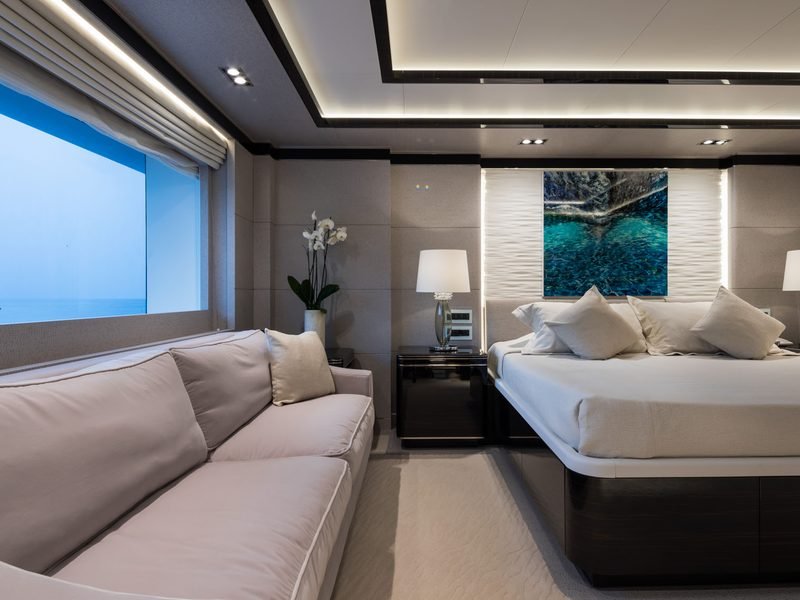 Master suite with bed against a textured wave panel and panoramic window at dusk
