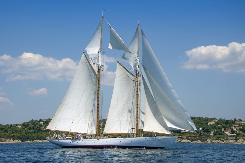Classic staysail schooner Puritan under full sail off a wooded Greek coastline