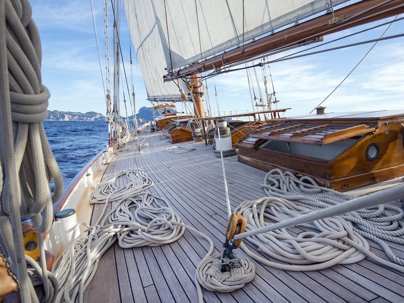 Teak foredeck underway with coiled halyards, varnished skylights and Capri's rocks ahead
