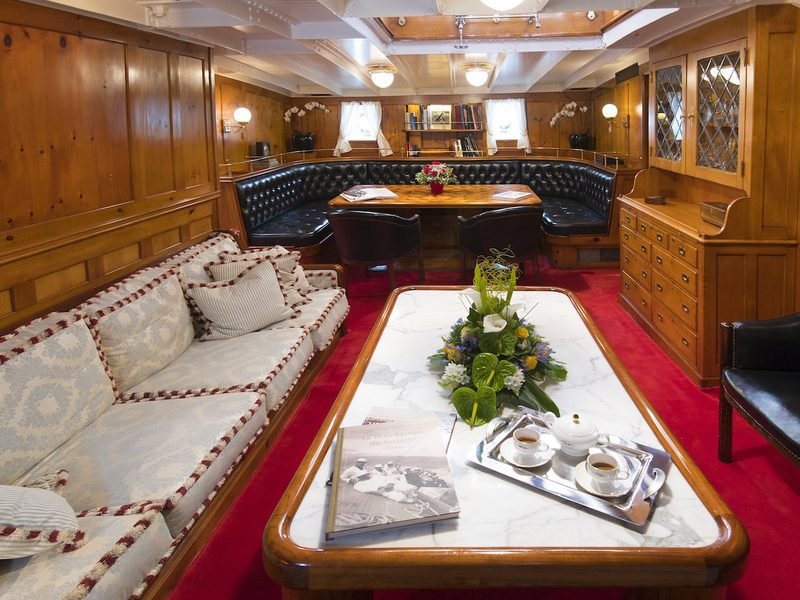 Main saloon with pine panelling, marble table, tufted leather banquette and aft library
