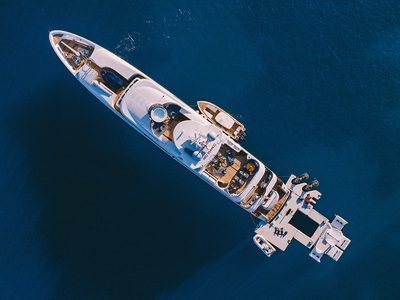 Overhead aerial of the white motor yacht at anchor, tender alongside on deep blue water