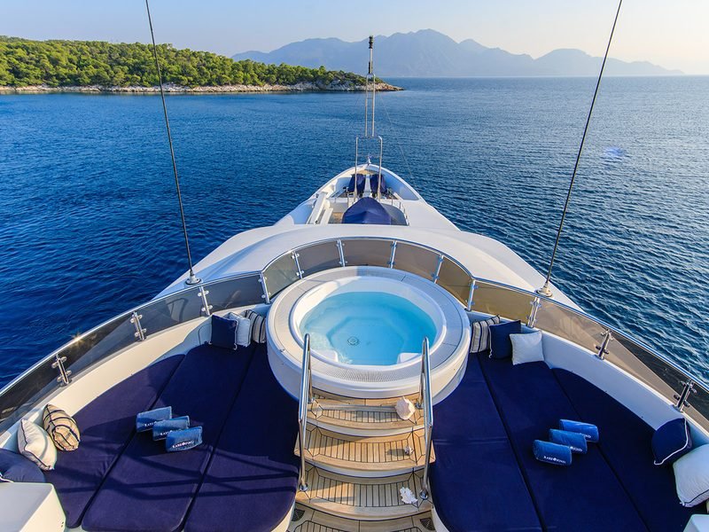 Foredeck jacuzzi ringed by navy sunpads, looking out over a calm island anchorage