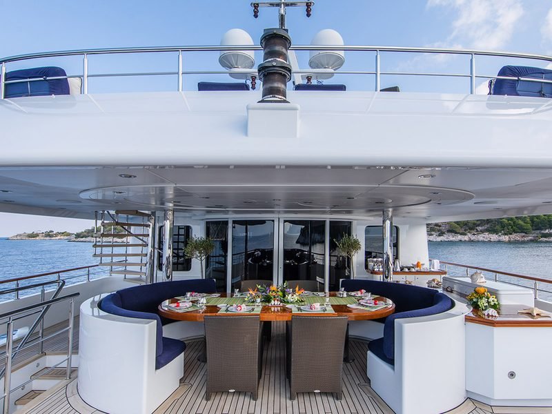 Aft deck dining table laid under the overhang, navy banquettes and open sea beyond