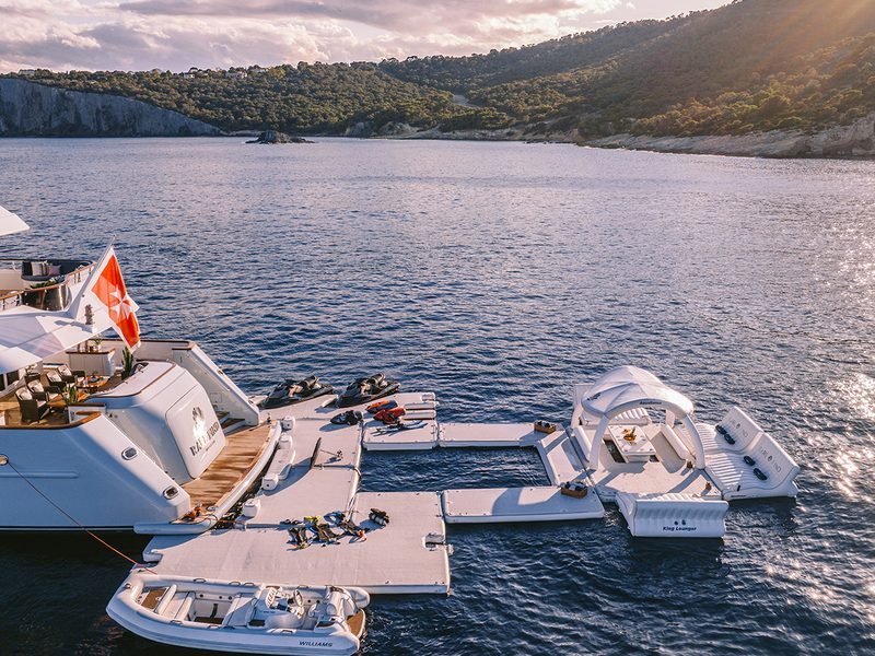 Beach club platform at golden hour with floating sea pool, jet skis and tender