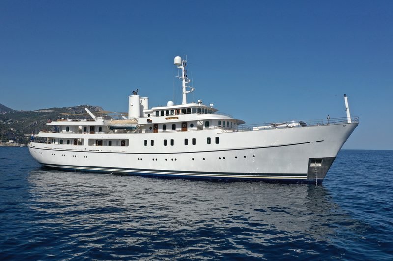 Classic white motor yacht lying at anchor off a sunlit Mediterranean headland, port profile