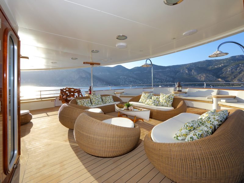 Shaded aft deck lounge with woven pod chairs, deck showers and mountain coastline