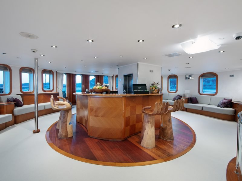 Main saloon with circular veneered bar, carved hand-form stools and grey banquettes