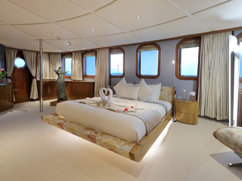Master stateroom with free-standing bed on a lit plinth and panoramic windows