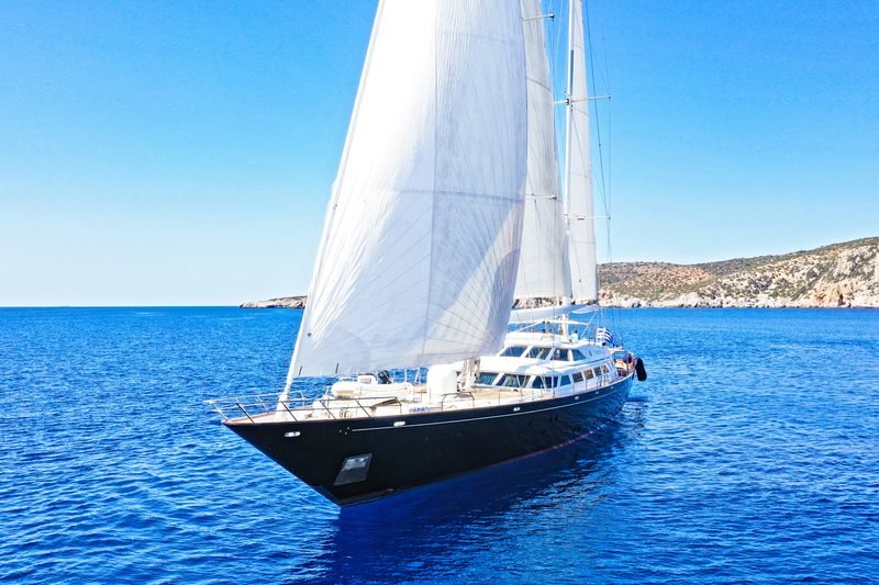 Sailing yacht under full main and headsail off a rocky Greek headland