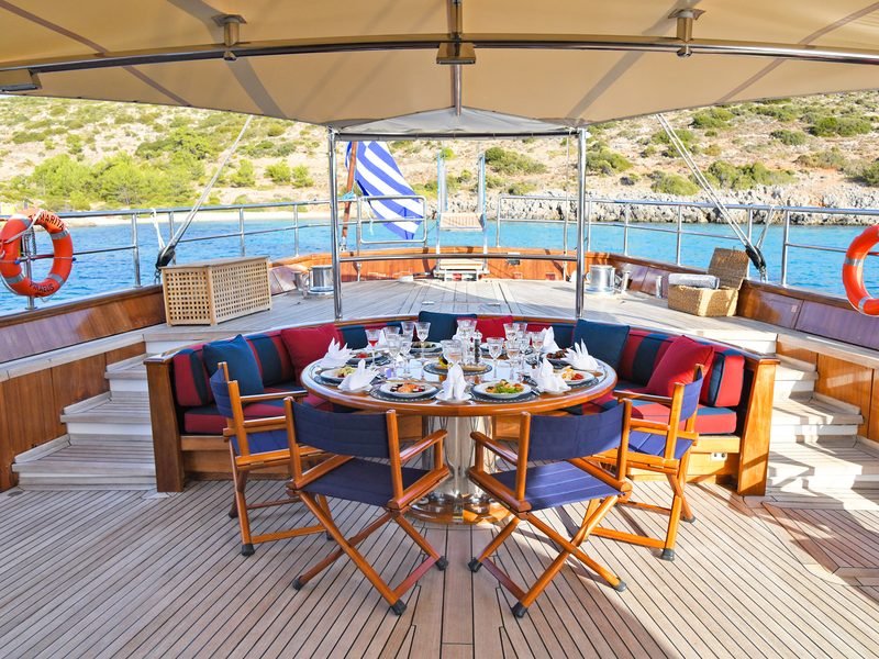 Aft-deck dining table laid with crystal beneath the awning, horseshoe banquette behind