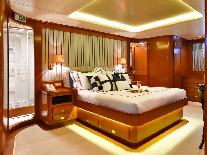 Master stateroom with centreline bed, cove-lit cherry joinery and en-suite shower beyond